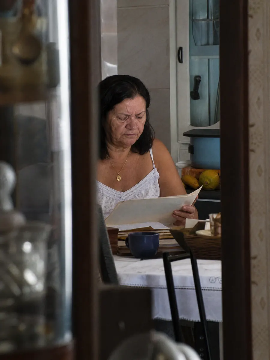 Servidora aposentada lendo documentos funcionais à mesa da cozinha