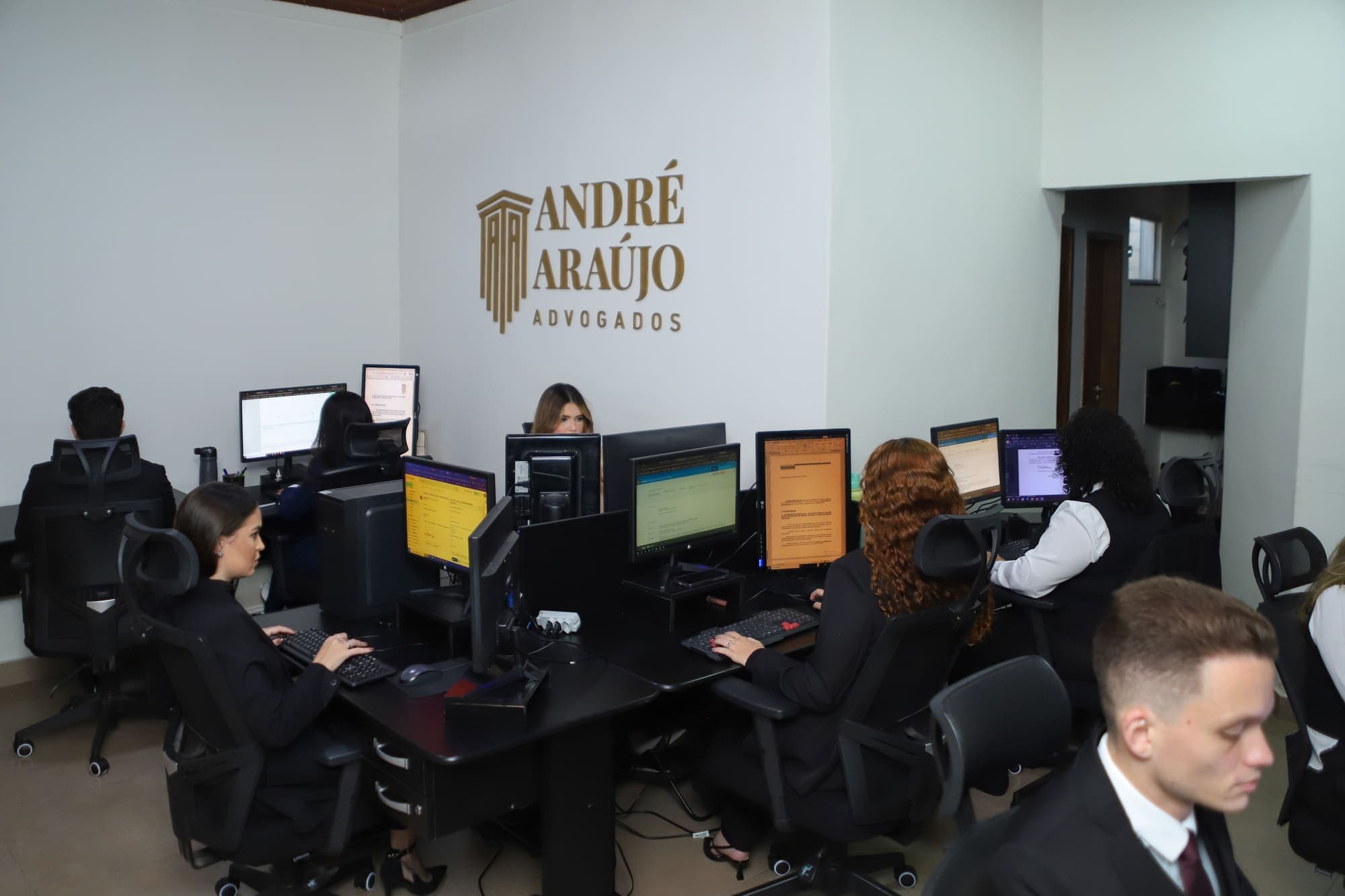 Equipe trabalhando nos computadores, sob o logotipo dourado na parede