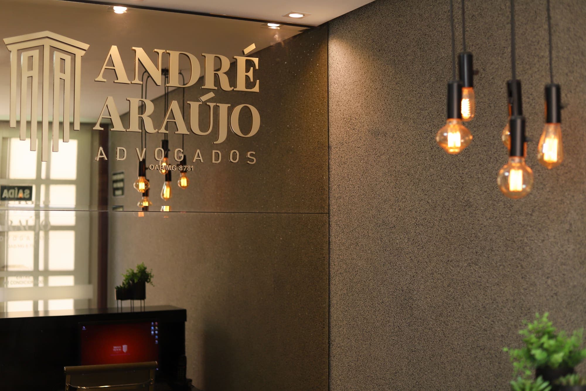 Painel da recepção com o logotipo dourado do André Araújo Advogados e luminárias de filamento