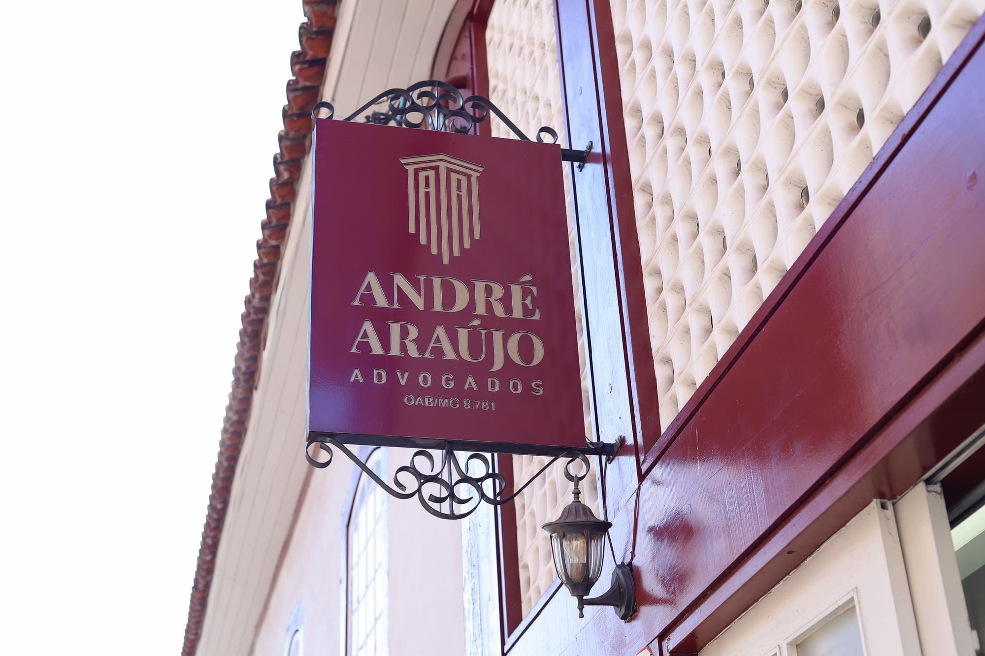 Placa vermelha com o logotipo dourado do escritório na fachada, ao lado da parede de cobogós