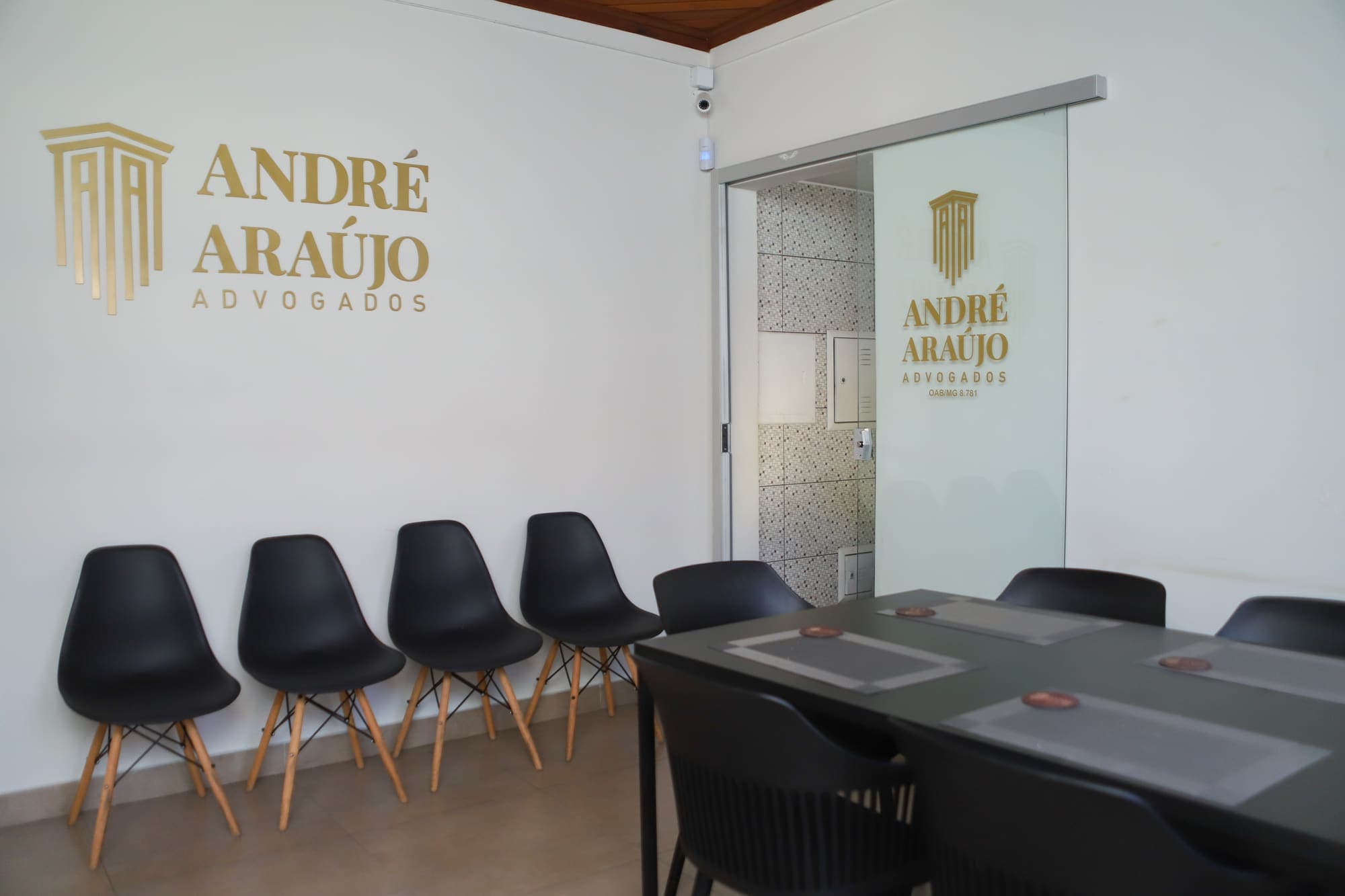 Sala de espera com cadeiras pretas e o logotipo do escritório na parede